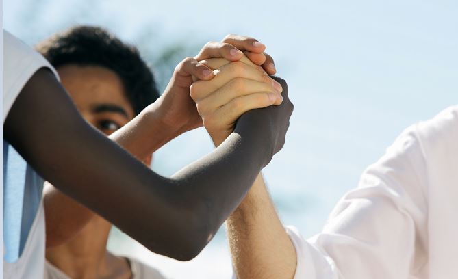 three hands from different race people clasping hands